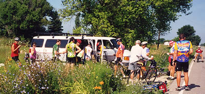 Group of riders at sag wagon stop on side of road.